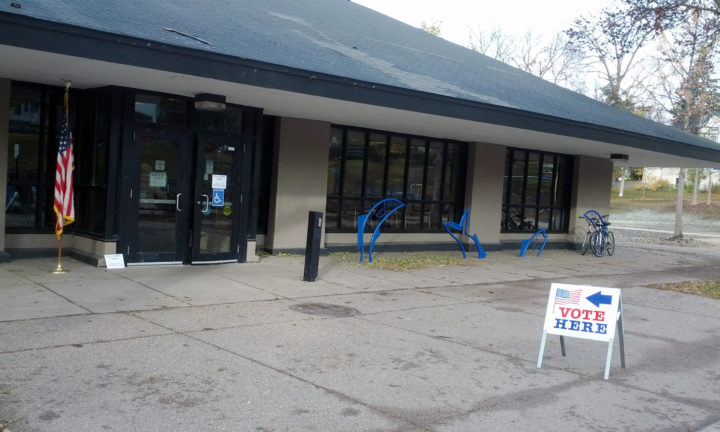 Photo outside polling place with sign reading, 'vote here' with arrow pointing to door