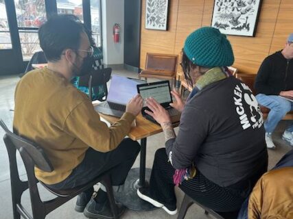 Two people sitting next to each other looking at two laptops.